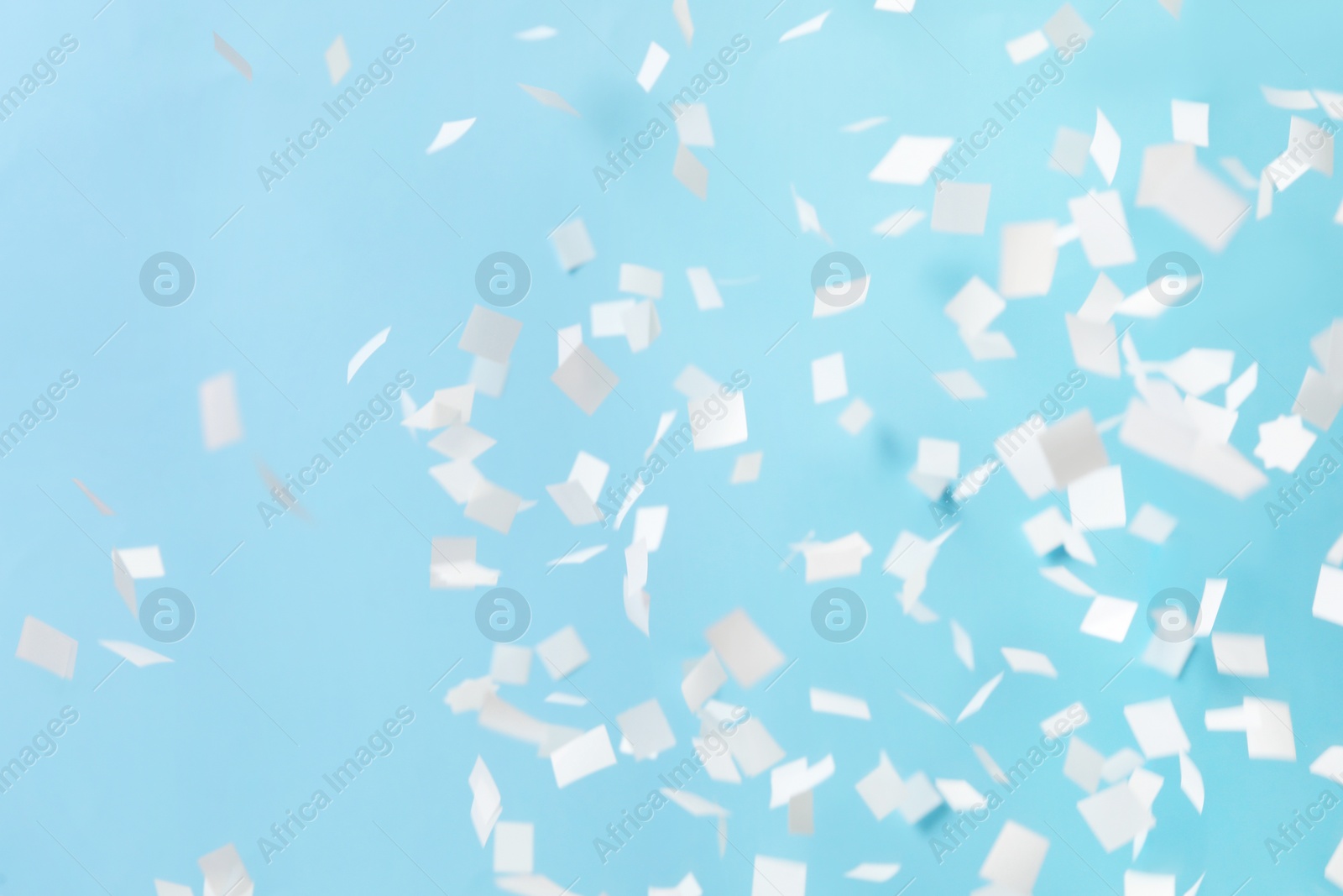 Photo of White confetti falling down on light blue background