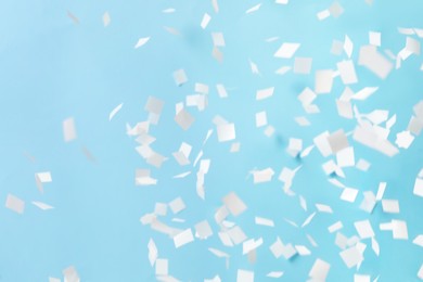 Photo of White confetti falling down on light blue background