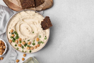 Photo of Delicious hummus with chickpeas and crispbread served on light grey table, flat lay. Space for text