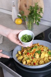 Photo of Woman adding cut green onion to rice with meat and vegetables in frying pan, closeup