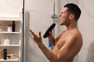 Photo of Man with bottle of gel singing in shower at home