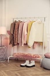 Rack with stylish warm clothes and shoes in modern dressing room