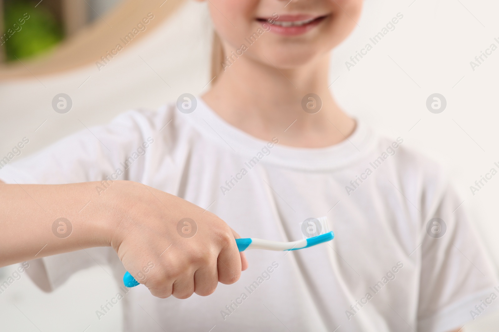 Photo of Little girl holding plastic toothbrush in bathroom, closeup