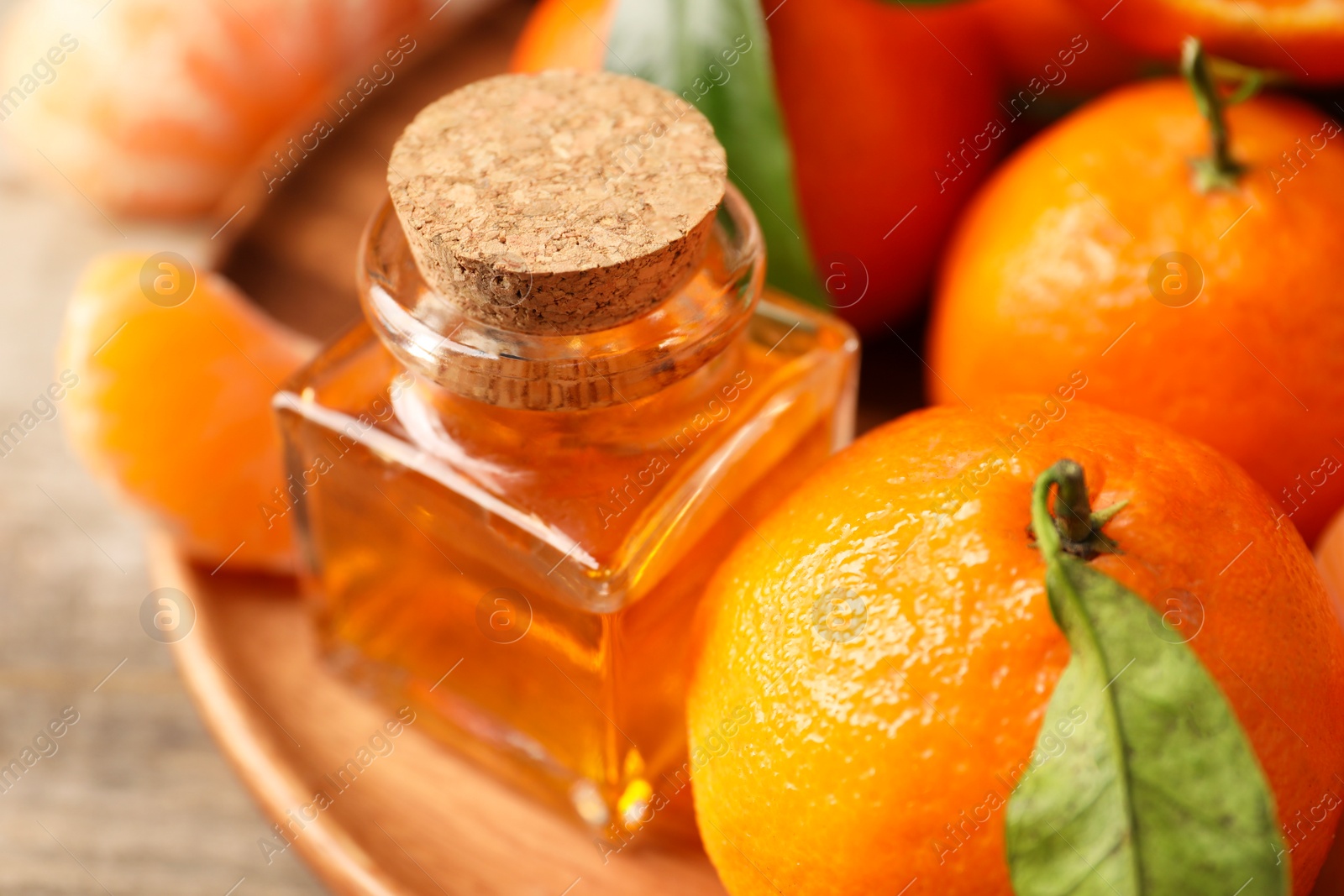 Photo of Bottle of tangerine essential oil and fresh fruits on wooden table, closeup