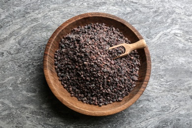 Photo of Black salt in bowl with scoop on grey table, top view