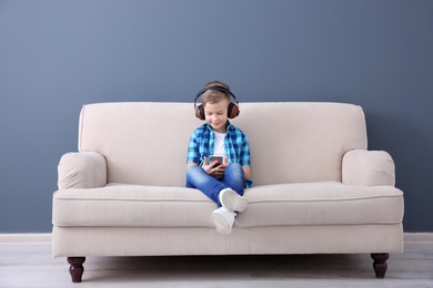 Photo of Cute little boy listening to music on sofa, indoors