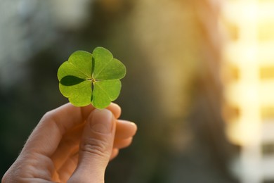 Photo of Woman holding beautiful green four leaf clover on blurred background, closeup. Space for text