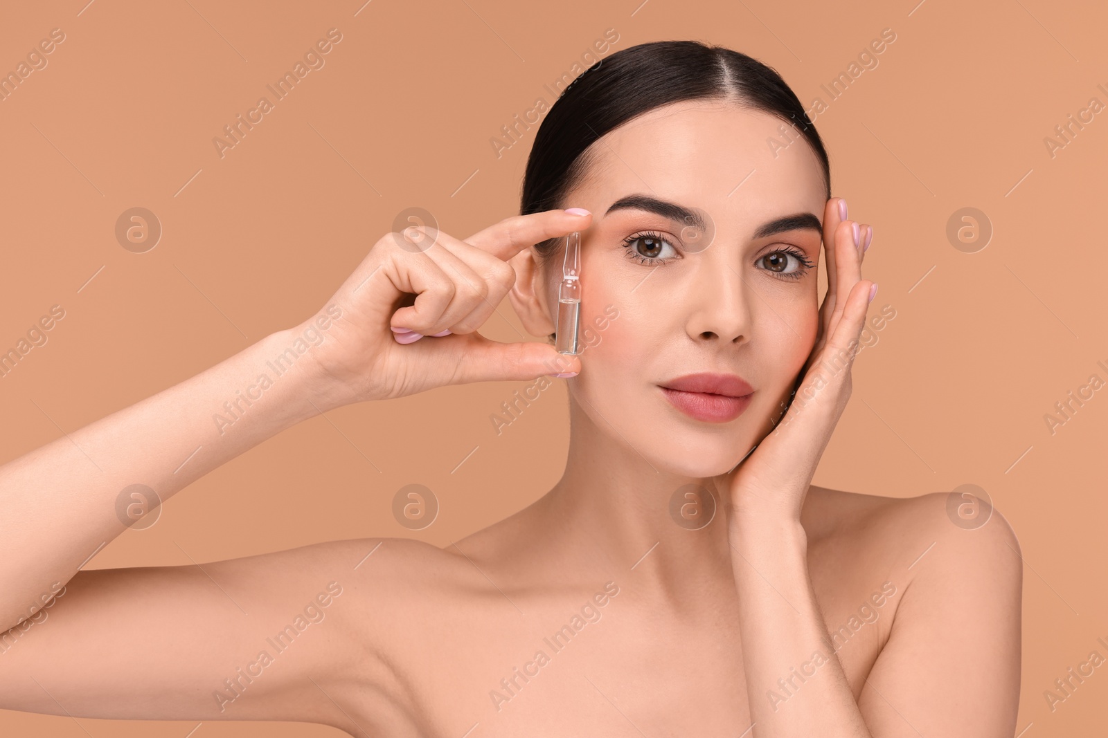 Photo of Beautiful young woman holding skincare ampoule on beige background