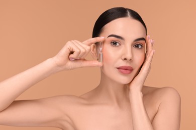 Beautiful young woman holding skincare ampoule on beige background