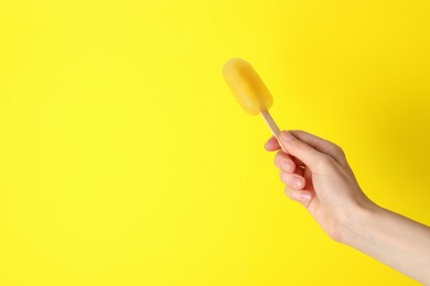 Photo of Woman holding delicious ice pop on yellow background, closeup view with space for text. Fruit popsicle