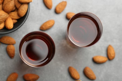 Photo of Glasses with tasty amaretto liqueur and almonds on gray table, flat lay
