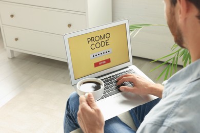 Photo of Man holding laptop with activated promo code and cup of coffee indoors, closeup