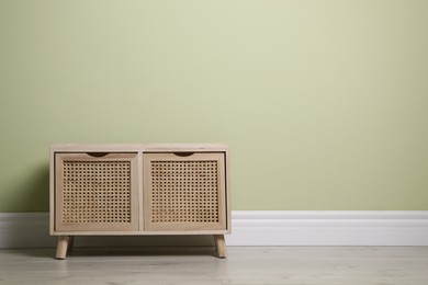 Modern wooden chest of drawers near light green wall indoors. Space for text