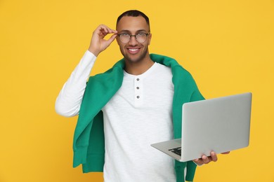 Photo of Happy young intern holding laptop on orange background