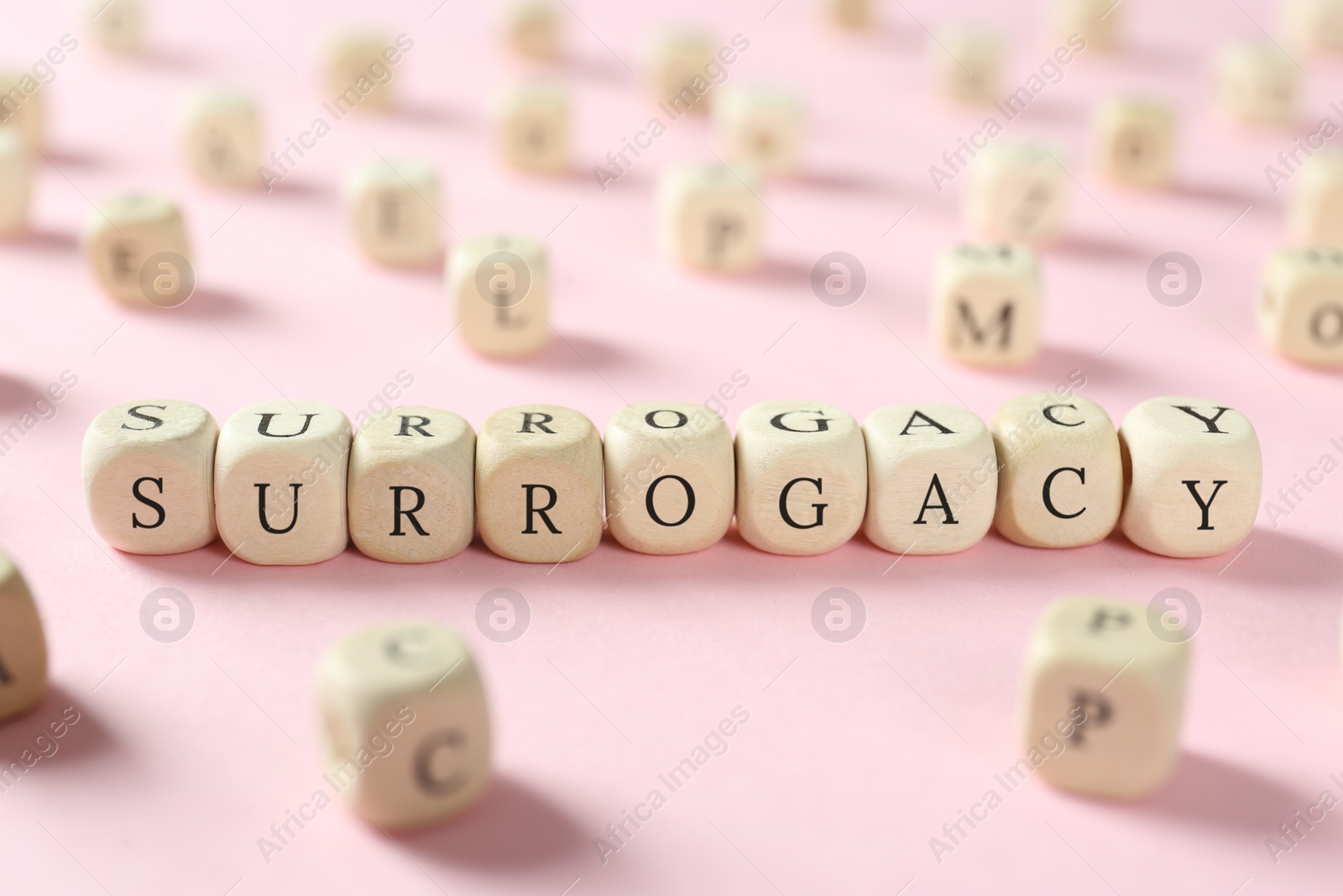 Photo of Word Surrogacy made of wooden cubes on pink background, closeup