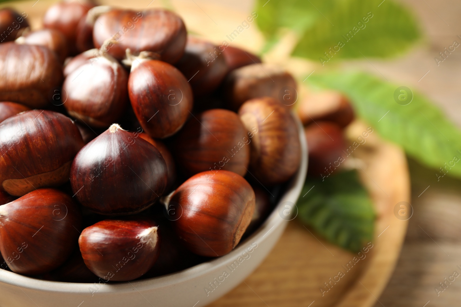 Photo of Fresh sweet edible chestnuts in bowl on table, closeup