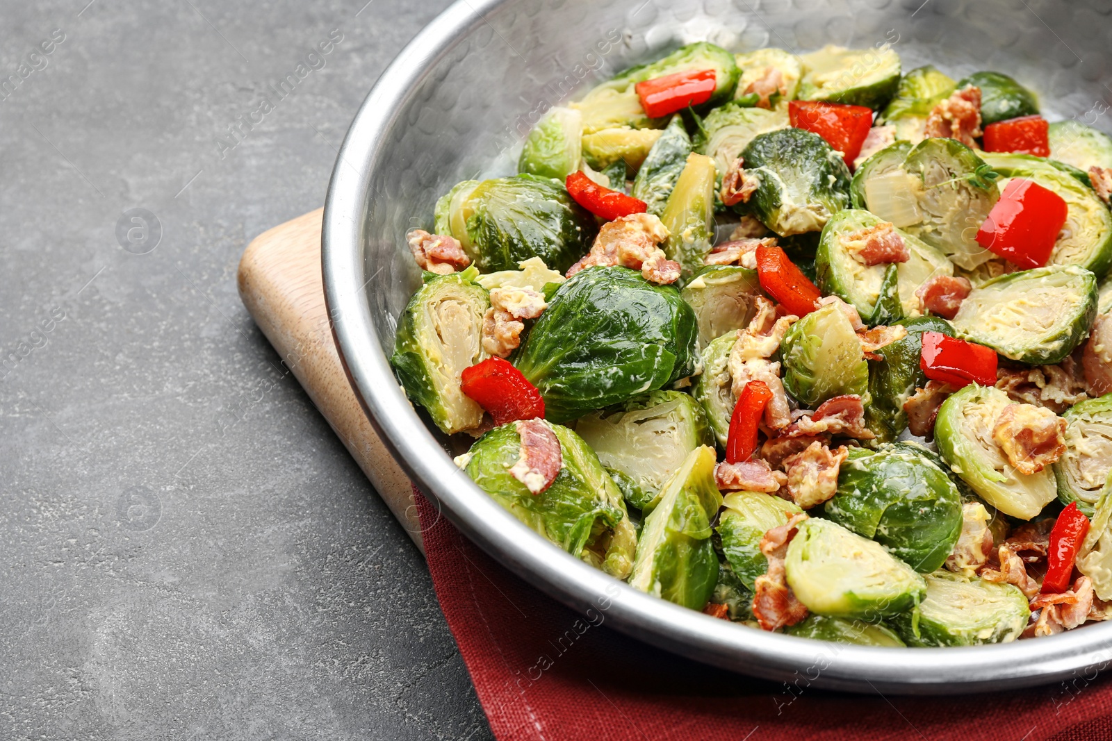 Photo of Delicious Brussels sprouts with bacon in pan on grey table, closeup