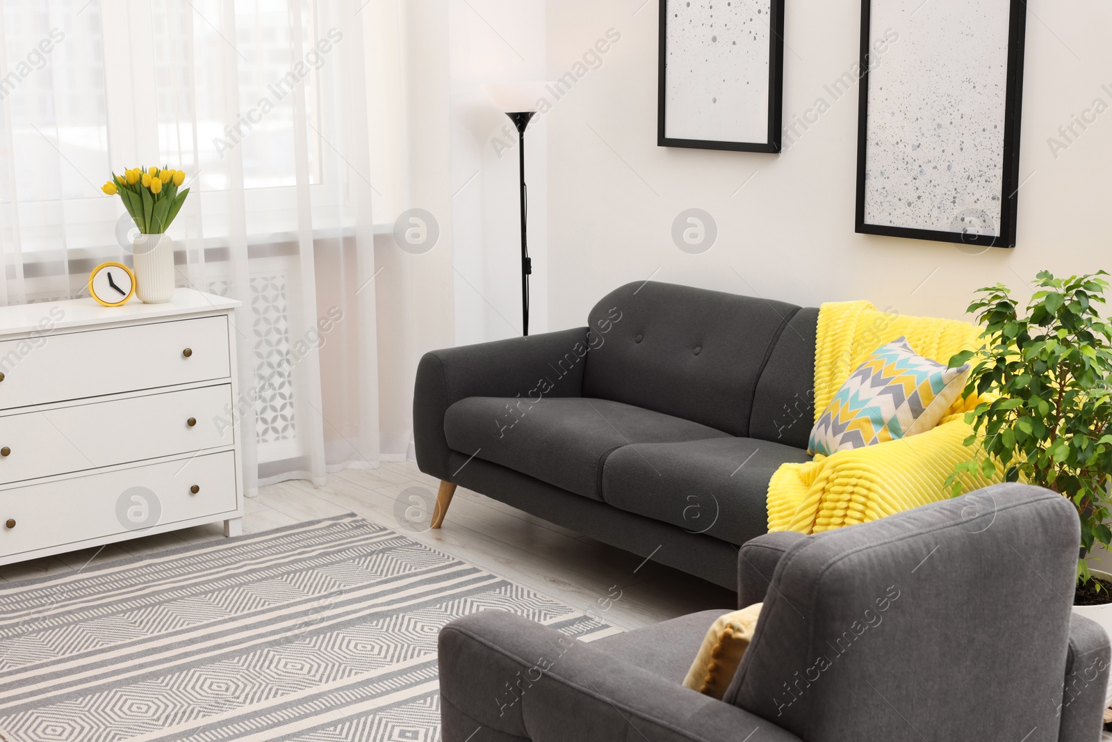 Photo of Spring atmosphere. Stylish living room interior with comfortable furniture and bouquet of beautiful yellow tulips