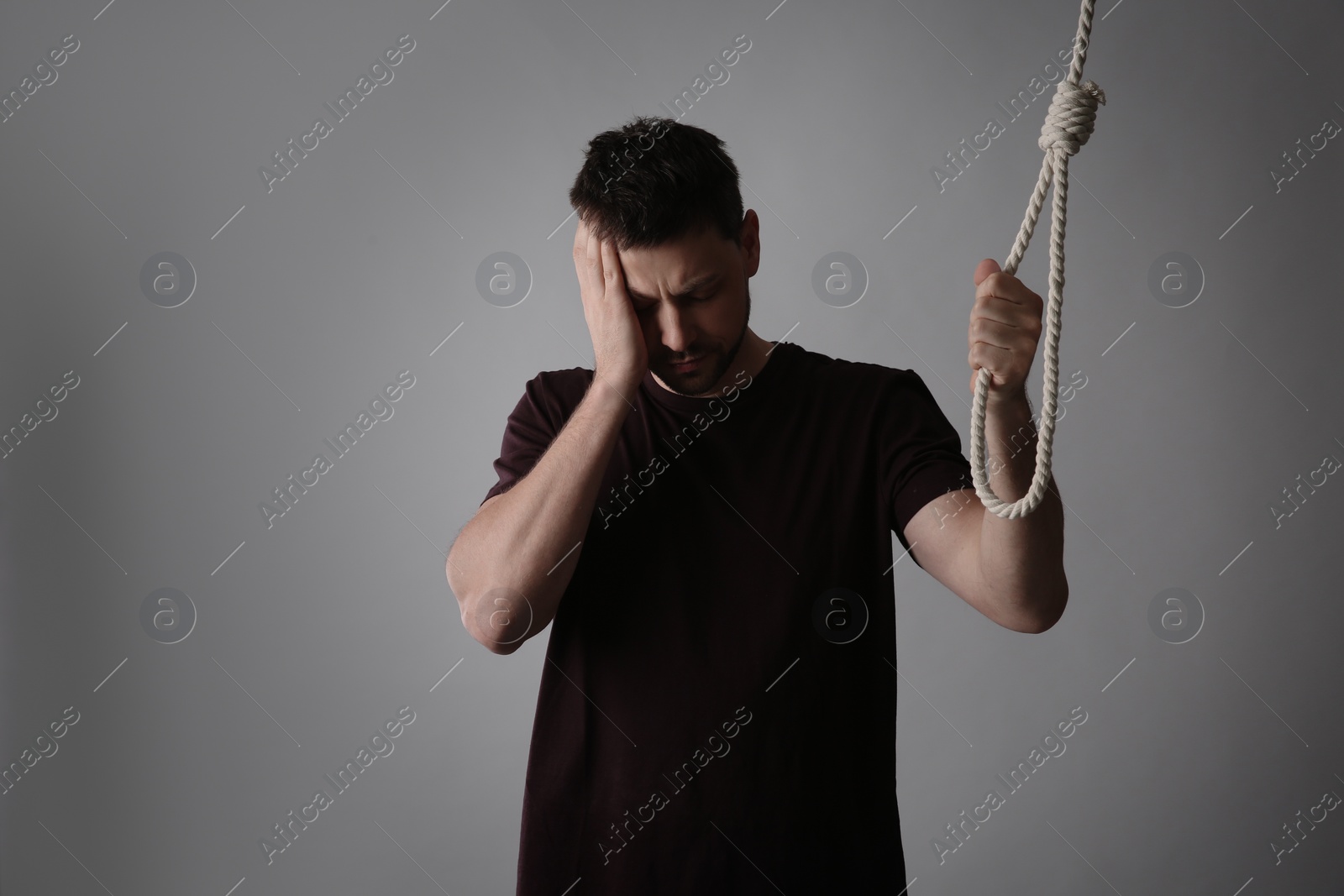 Photo of Depressed man with rope noose on light grey background