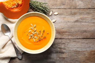 Photo of Flat lay composition with bowl of pumpkin soup and space for text on wooden background