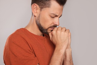Photo of Man with clasped hands praying on light grey background, closeup