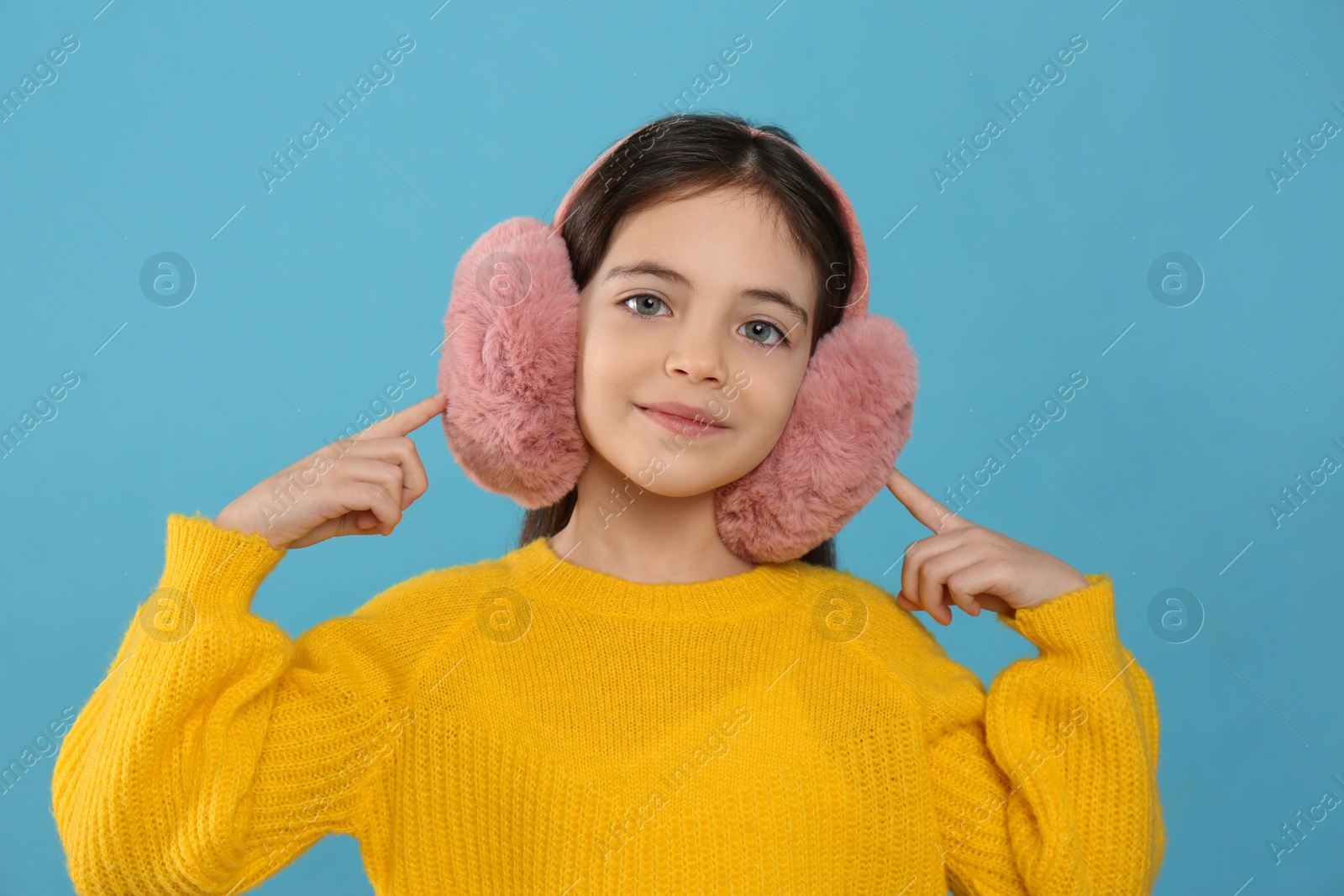 Photo of Cute little girl wearing stylish earmuffs on light blue  background