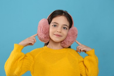 Photo of Cute little girl wearing stylish earmuffs on light blue  background