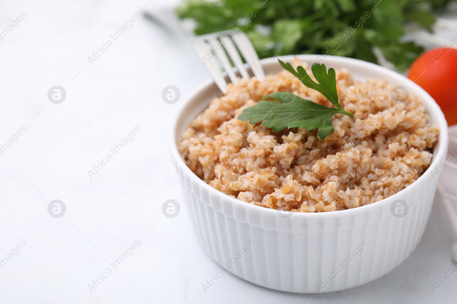 Photo of Tasty wheat porridge with parsley in bowl on white table, closeup. Space for text