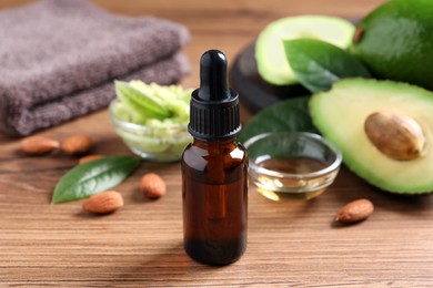 Photo of Bottle of essential oil, fresh avocado and almonds on wooden table