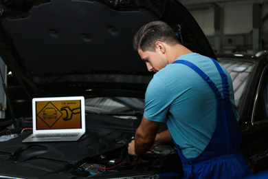 Photo of Mechanic with laptop doing car diagnostic at automobile repair shop
