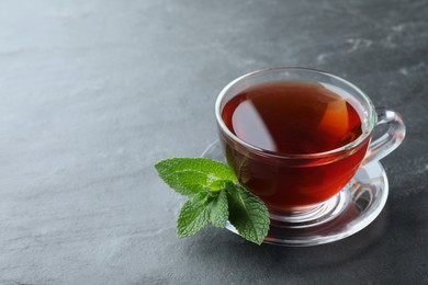 Photo of Cup of hot aromatic tea with mint on grey table. Space for text