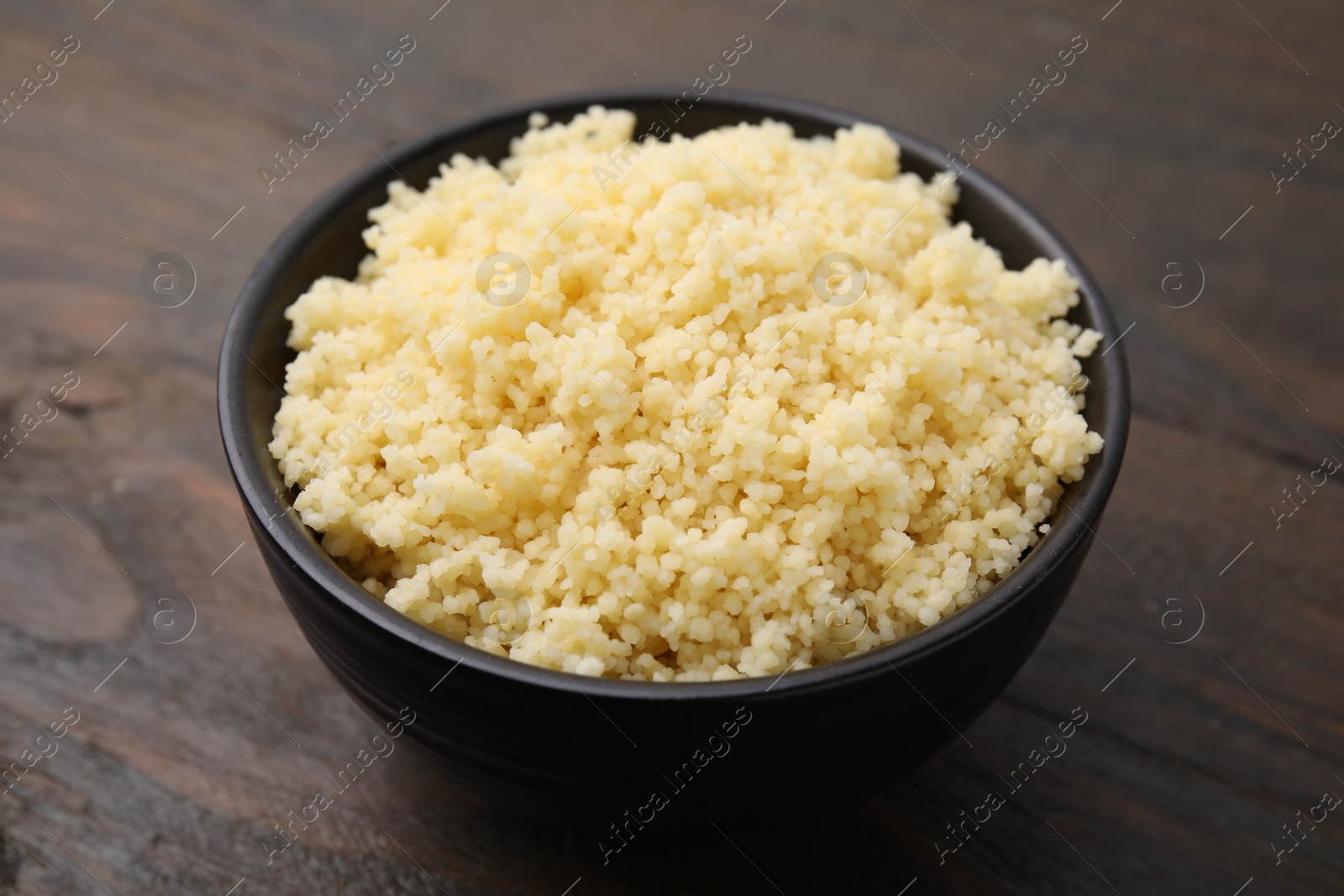 Photo of Tasty couscous in bowl on wooden table, closeup