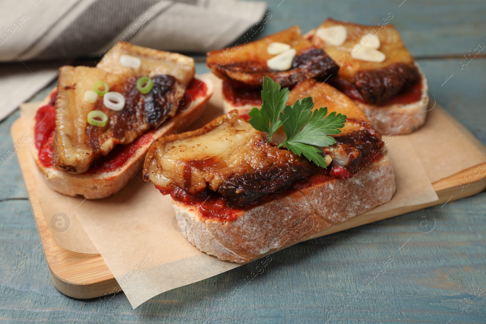 Photo of Tasty sandwiches with fried pork fatback slices on light blue wooden table