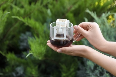 Photo of Woman holding cup with drip coffee bag outdoors, closeup
