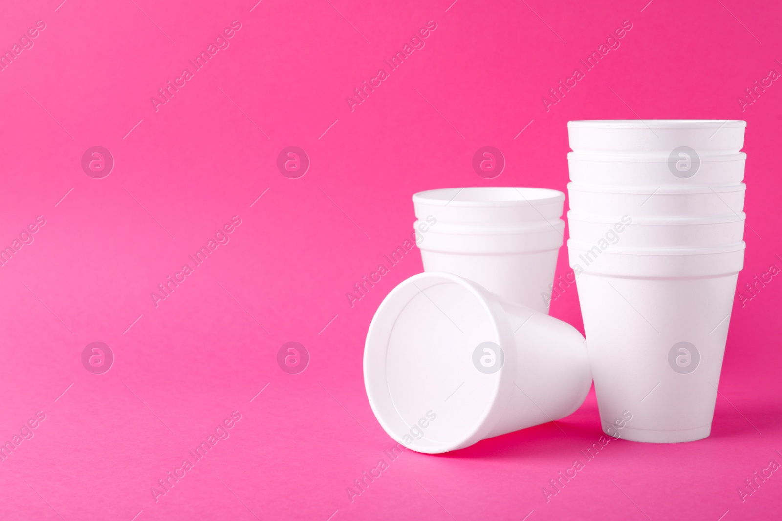 Photo of White styrofoam cups on pink background, space for text