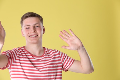 Photo of Happy teenage boy taking selfie on yellow background