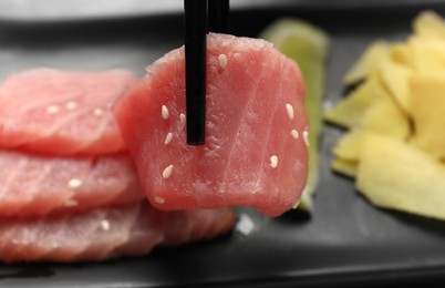 Photo of Taking tasty sashimi (piece of fresh raw tuna) from black plate, closeup