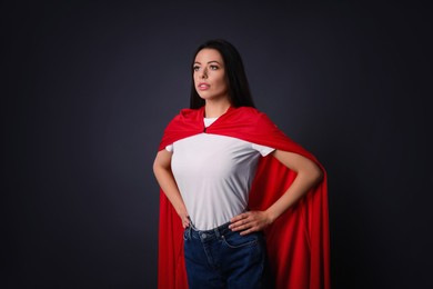Photo of Confident young woman wearing superhero cape on grey background