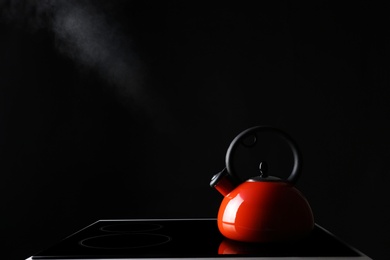 Modern kettle with whistle on stove against black background, space for text