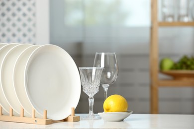 Photo of Clean plates in dish drying rack, glasses and lemon on white table indoors