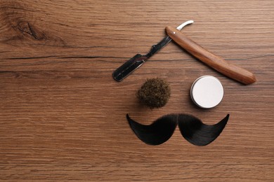 Artificial moustache and barber tools on wooden table, flat lay. Space for text