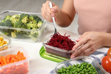 Photo of Woman preparing cut beetroot for freezing and containers with fresh products on white table, closeup. Food storage