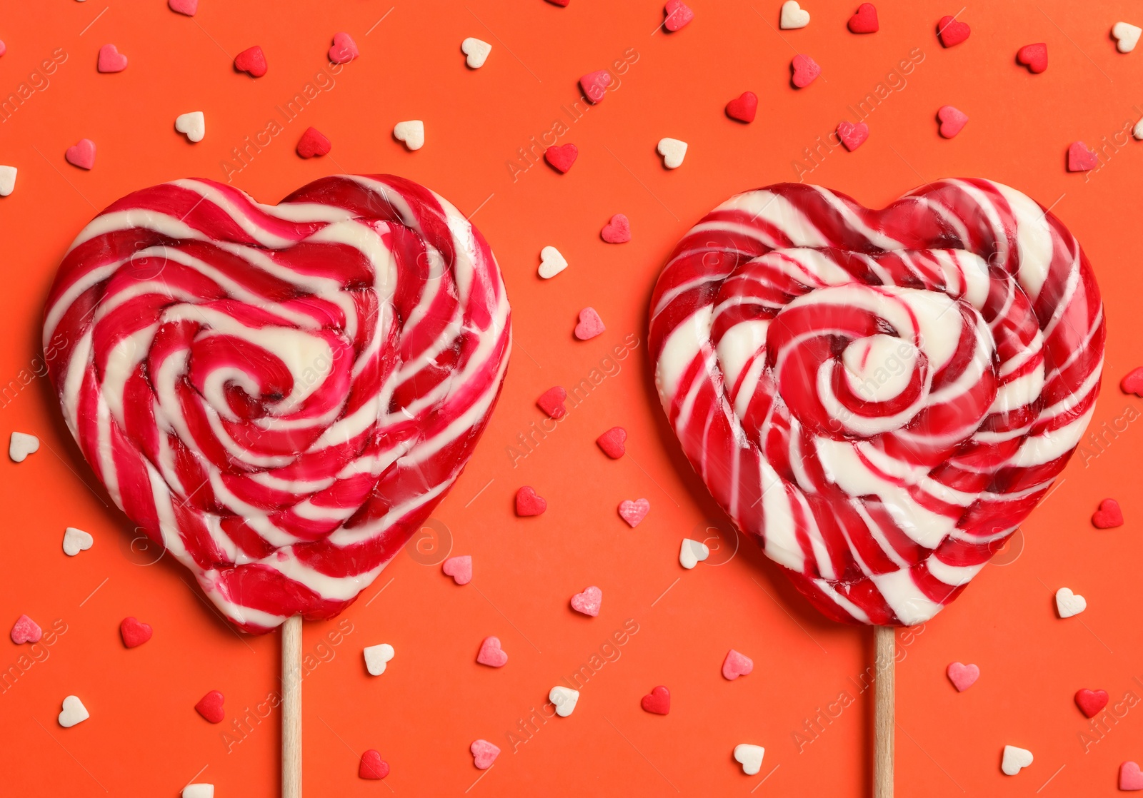 Photo of Sweet heart shaped lollipops and sprinkles on coral background, flat lay. Valentine's day celebration