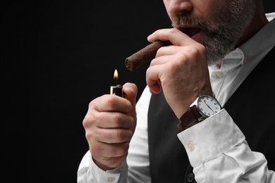 Man lighting cigar on black background, closeup. Space for text