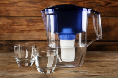 Filter jug and glasses with purified water on wooden table