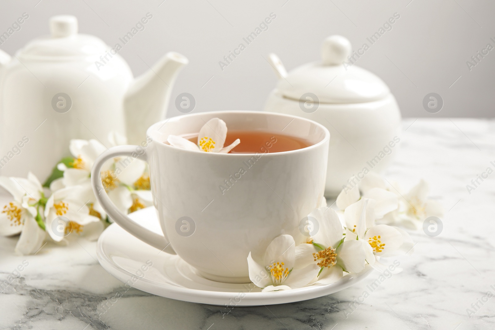 Photo of Aromatic jasmine tea and fresh flowers on white marble table
