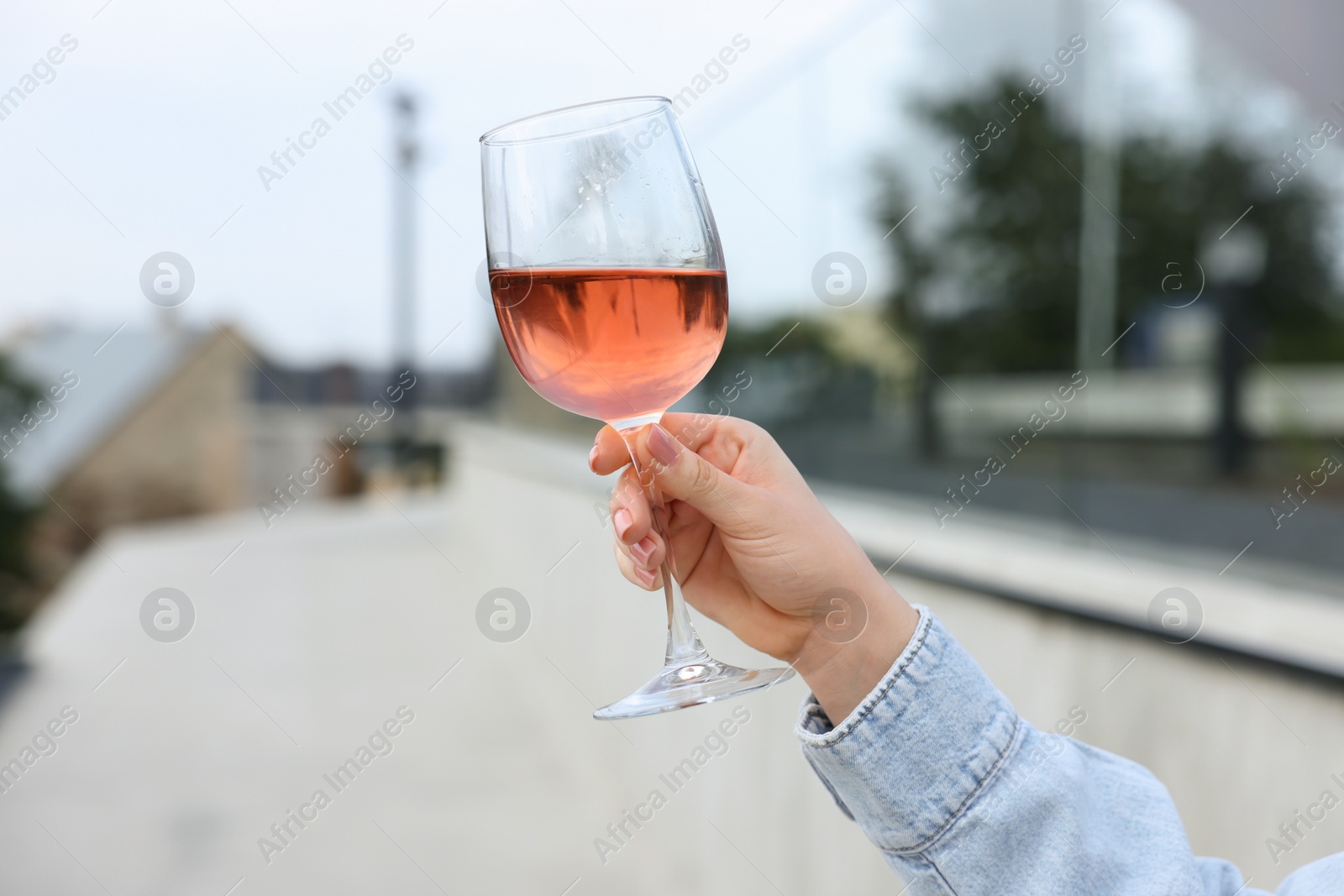 Photo of Woman holding glass of rose wine outdoors, closeup