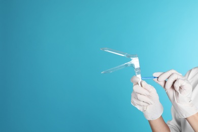 Photo of Female doctor holding vaginal speculum on color background, closeup view with space for text. Medical object