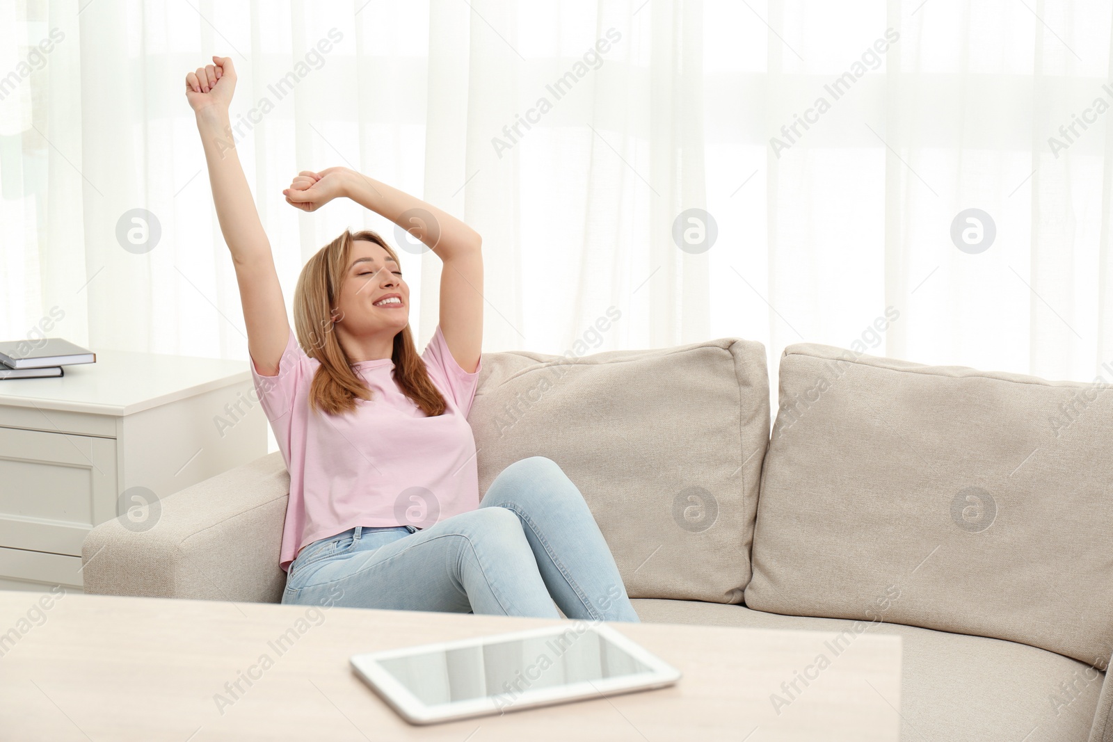 Photo of Beautiful young woman stretching on sofa at home, space for text