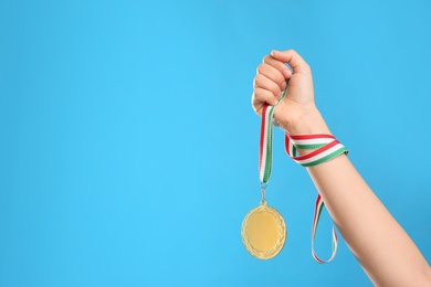 Woman holding gold medal on light blue background, closeup. Space for text